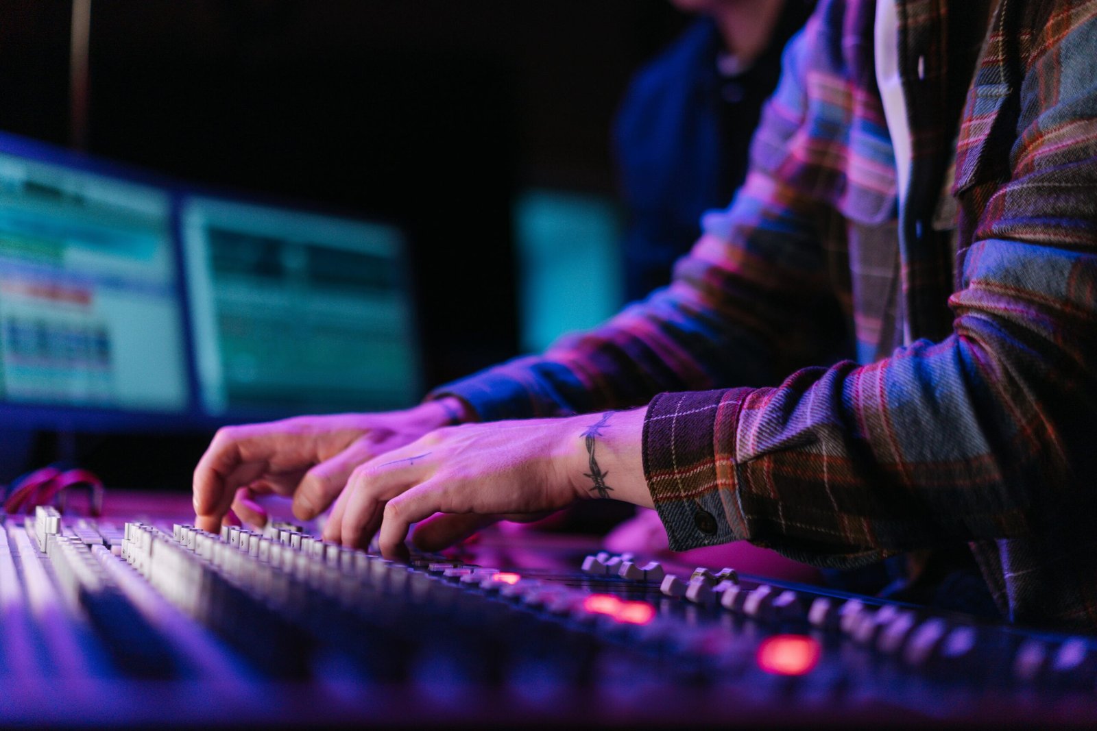 Close-up of hands adjusting an audio mixer in a neon-lit studio environment.